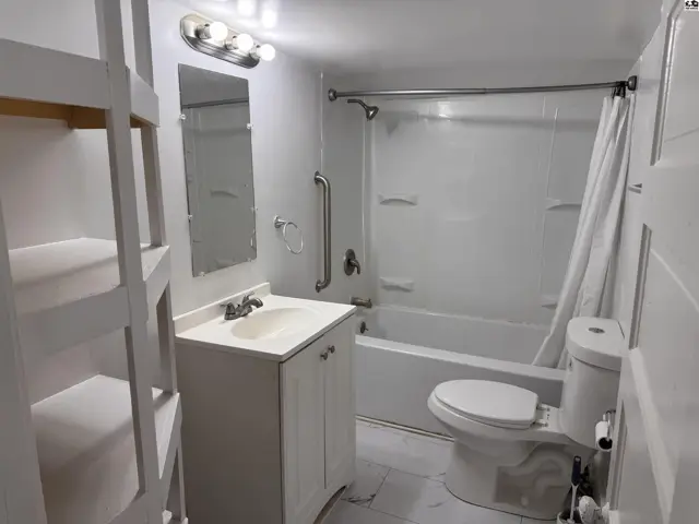 Bright white bathroom features a vanity, toilet, tub/shower combo, and built-in shelving.