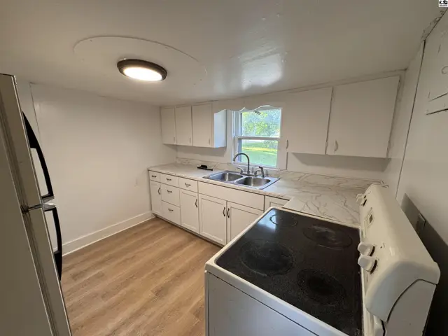 Bright kitchen with white cabinets, stainless steel appliances, and light wood-look flooring.