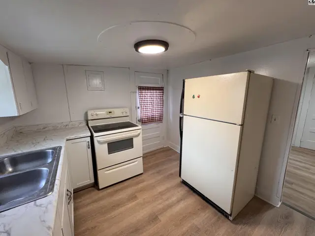 Kitchen with white cabinets, stainless steel sink, beige stove, and refrigerator on wood-look flooring.