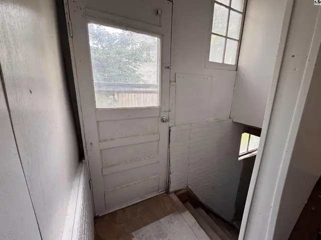 A narrow, white-painted entryway with a paneled door, brick wainscoting, and a small window.