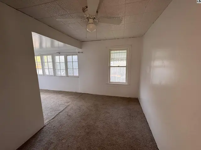 Living room with textured ceiling, carpet, and a ceiling fan, opening to a sunroom.
