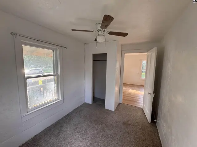 Bedroom with plush carpet, white walls, ceiling fan, and an open doorway to another room.