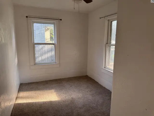 Cozy bedroom with neutral carpet, white walls, and two windows letting in natural light.