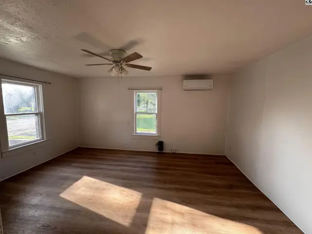 Spacious living room with wood-look flooring, ceiling fan, and mini-split AC unit.