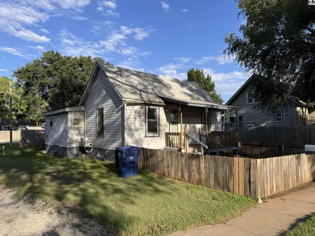 Exterior of a weathered gray wood-sided house with a wooden fence and porch.