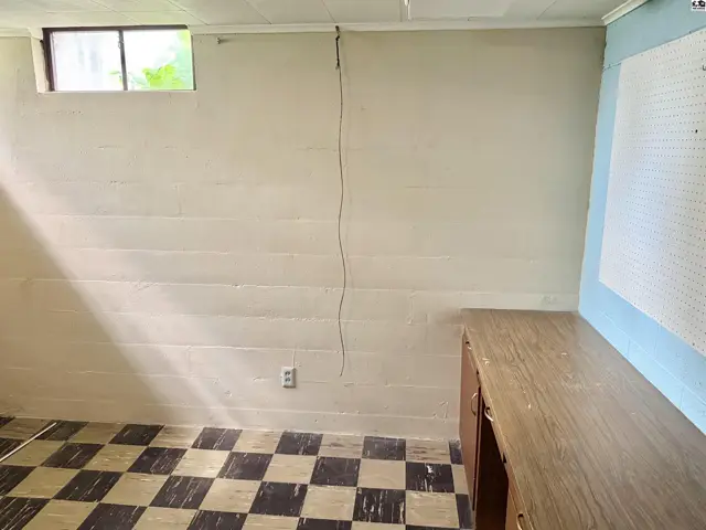 Basement room with checkered floor, painted block walls, and a wooden desk.