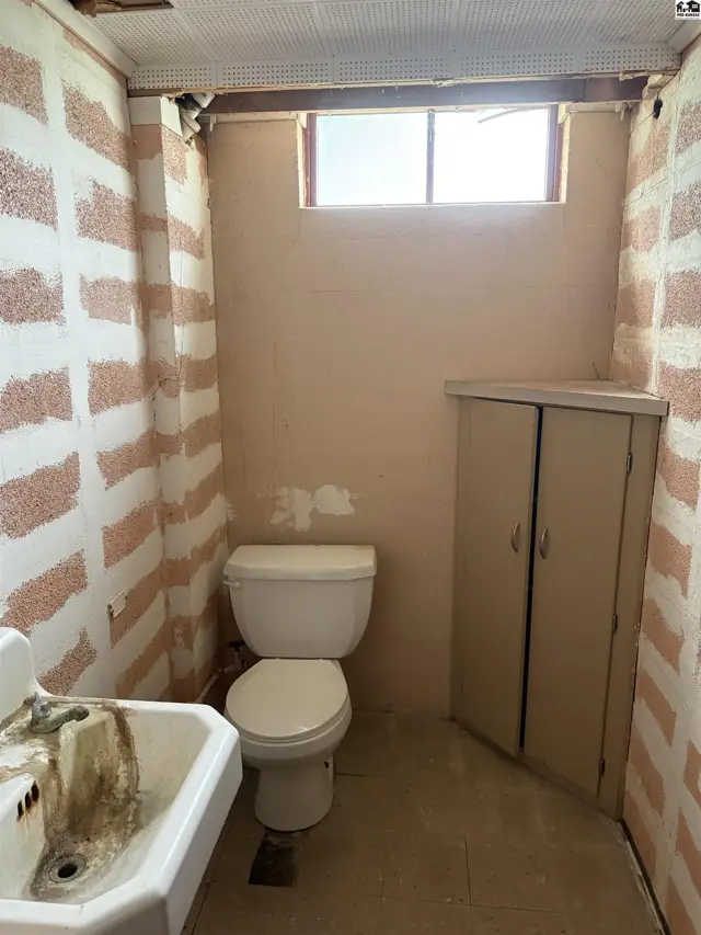 Small bathroom with a toilet, sink, and corner cabinet, featuring textured walls and a small window.