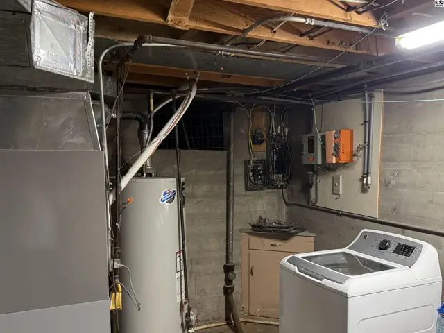 Concrete basement with water heater, furnace, washer, and exposed ceiling joists.