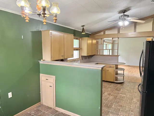 Kitchen with light wood cabinets, green accent wall, and vaulted ceiling with exposed beams.