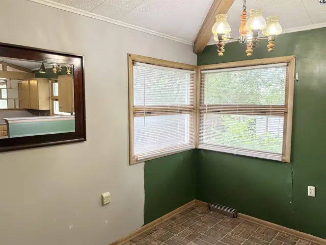 Corner dining area with green and beige walls, wood-trimmed windows, and a mirrored wall reflecting a kitchen.