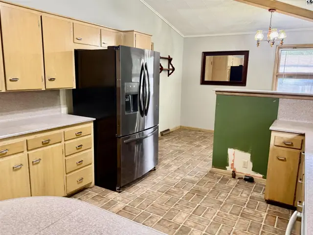 Kitchen with light wood cabinets, stainless steel refrigerator, and patterned tile flooring.