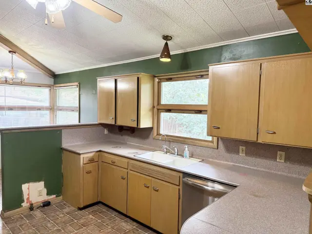 Kitchen with light wood cabinets, white sink, and green walls under a vaulted ceiling.