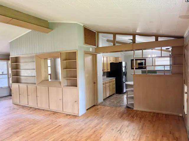 Spacious living area with built-in light wood shelving and cabinets, opening to a kitchen with wood cabinets.