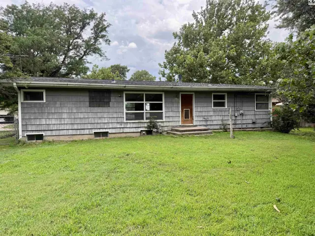 Gray shingle-sided ranch home with a red door and large windows sits on a grassy lawn.