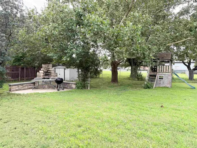 Spacious backyard features a stone outdoor kitchen, shed, and a wooden playset with slide.