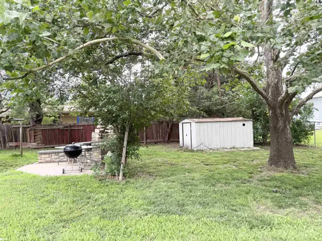 Spacious backyard with a built-in stone grill, white storage shed, and mature trees.