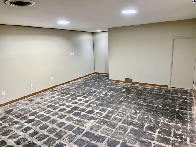 Spacious room with beige walls, wood trim, and a floor needing new flooring.