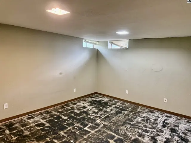 Unfinished basement room with concrete floor, beige walls, and small windows.