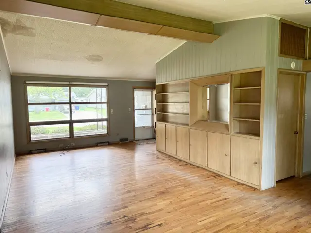 Spacious living room with vaulted ceiling, large windows, and built-in wood cabinetry.