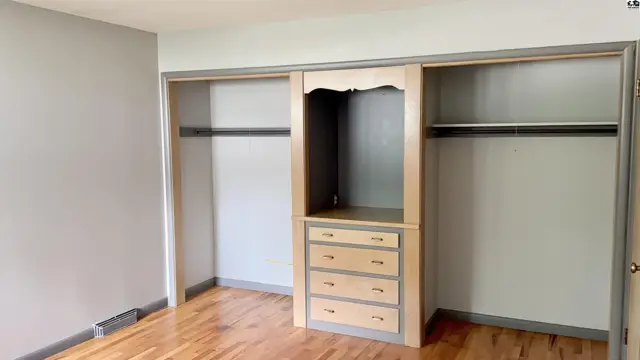 Spacious bedroom with hardwood floors and a built-in dresser between two large closets.