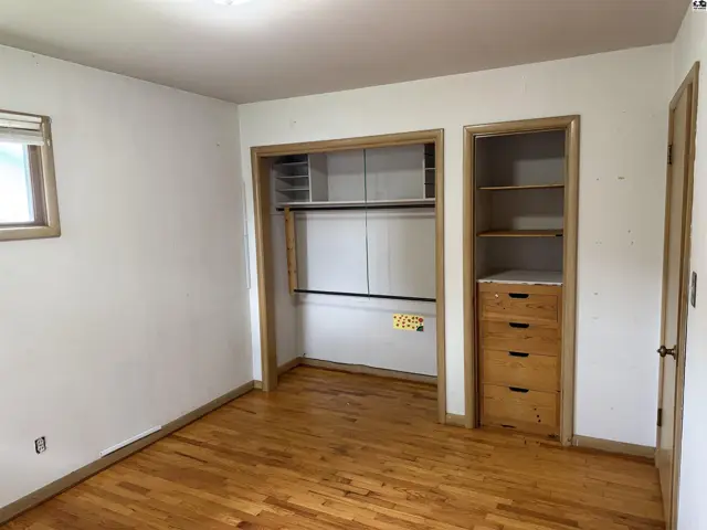 Spacious bedroom with hardwood floors and built-in closets featuring shelving and drawers.