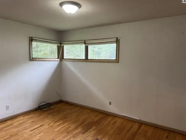 Corner bedroom with hardwood floors and three windows offering natural light.