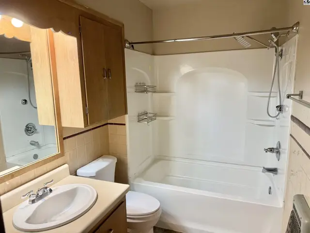Bathroom with white tub, vanity, toilet, and wood cabinetry.