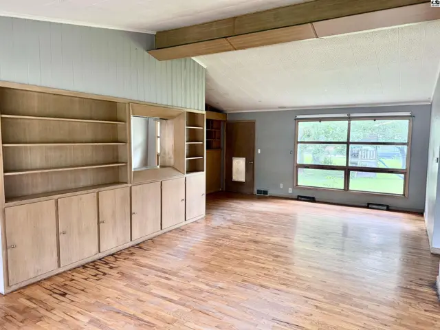 Spacious living room with vaulted ceiling, built-in wood cabinetry, and large windows overlooking the yard.