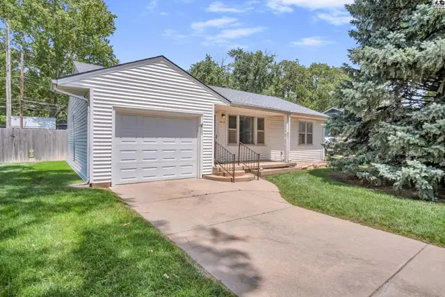 White vinyl-sided ranch home with a two-car garage and mature trees on a sunny day.