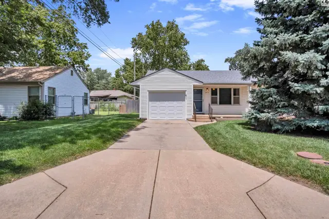 Charming white bungalow with attached garage, concrete driveway, and manicured lawn.