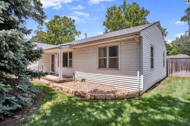 Exterior view of a white vinyl-sided ranch home with a covered porch and mature trees.