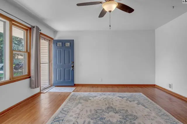 Spacious living room with hardwood floors, a blue front door, and a large area rug.