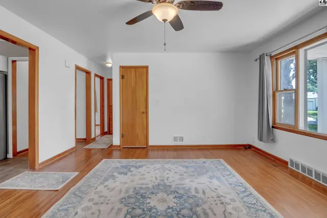 Spacious living room with hardwood floors, a patterned rug, white walls, and a ceiling fan.