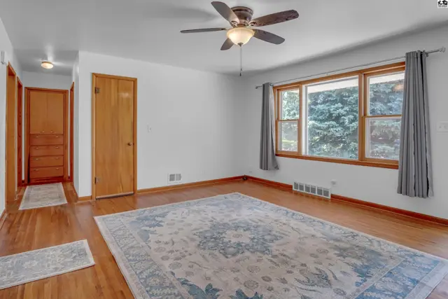 Spacious living room with hardwood floors, large window, ceiling fan, and a decorative rug.
