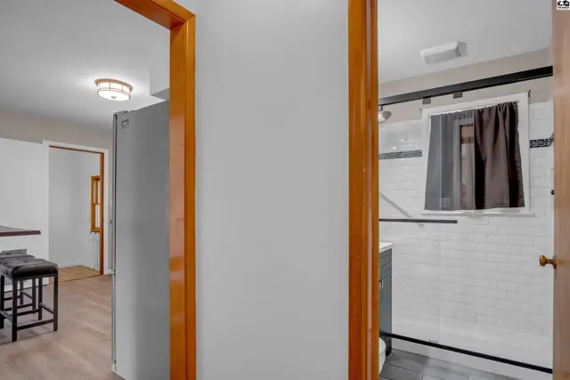 Modern bathroom with subway tile shower and dark hardware, visible from a hallway with wood trim.