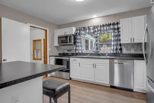 Modern kitchen with white cabinets, stainless steel appliances, granite countertops, and wood-look flooring.