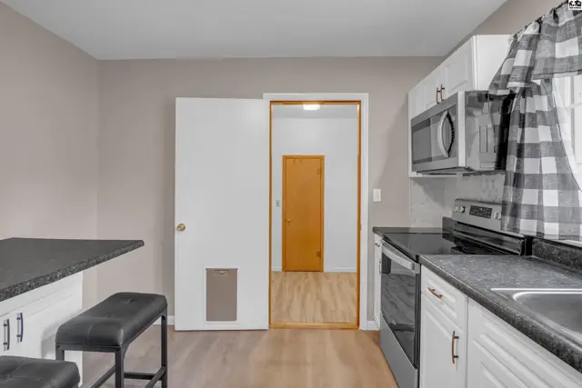 Modern kitchen with white cabinets, granite countertops, stainless steel appliances, and a breakfast bar.