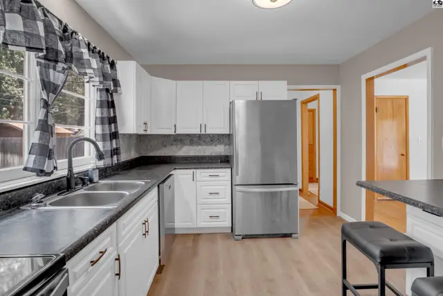 Modern white kitchen with stainless steel appliances, granite countertops, and wood-look flooring.