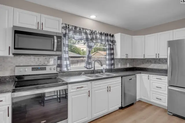 Modern white kitchen with stainless steel appliances, granite countertops, and checkered curtains.