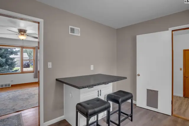 Modern kitchen island with dark countertop and two black stools, adjacent to a living room.