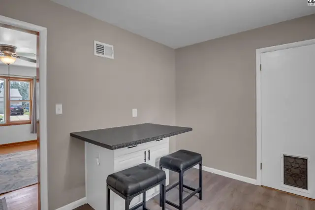 Kitchen island with granite countertop and two black stools, adjacent to a doorway and a white door.