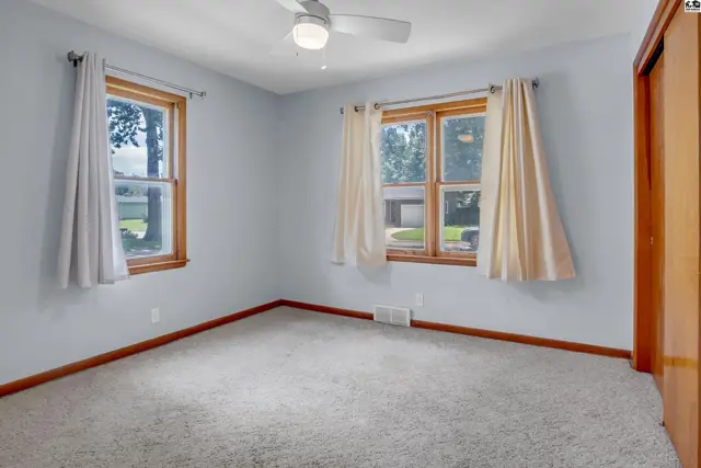 Light-filled bedroom with neutral carpet, light blue walls, wood trim, and a closet.