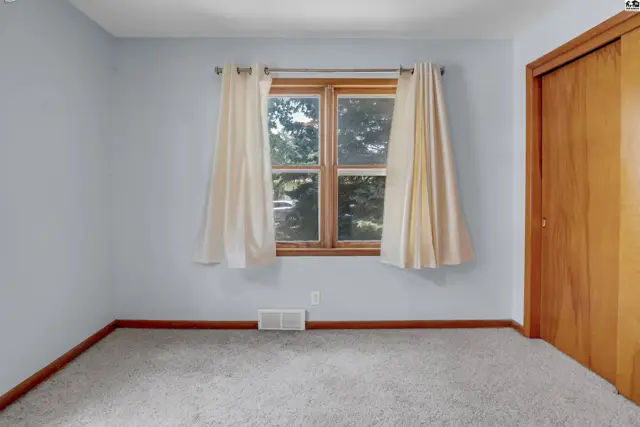 Light blue bedroom with a large window, cream curtains, and a wooden closet door.