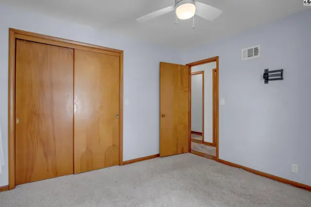 Light blue bedroom with wood-paneled closet doors, light carpet, and a ceiling fan.