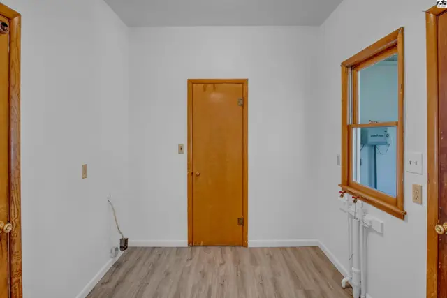Interior view of a room with white walls, wood door, and a window with wooden trim.