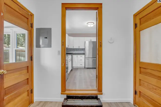 View through a wooden doorway into a bright kitchen with white cabinets and stainless steel appliances.