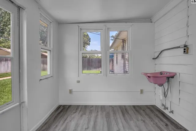 Sunlit utility room with pink sink, white paneled walls, and wood-look flooring.
