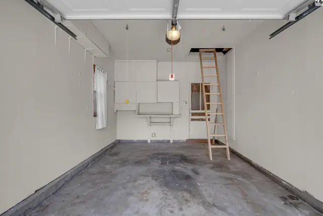 Spacious garage with concrete floor, white cabinets, and a wooden ladder leading to storage.