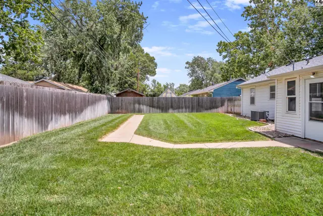 Spacious backyard with a paved walkway, lush green grass, and a tall wooden fence.