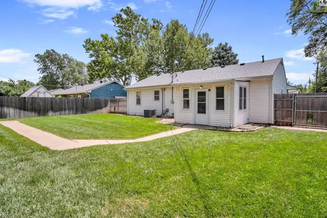 White siding home with a large green lawn, concrete path, and wooden fence under a blue sky.